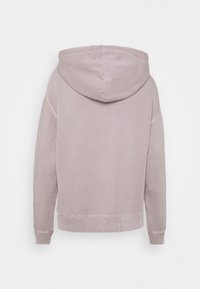 Mikina s kapucí vyrobená z jemného, světle růžového materiálu. Disponuje uvolněným střihem, žebrovanými manžetami a lemem. Zádový pohled s viditelnými švy.