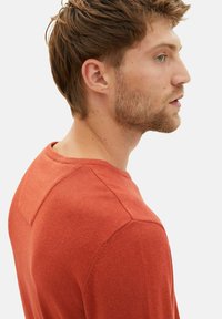 Suéter de punto color óxido con cuello redondo y una costura en la parte posterior. La tela parece suave y con textura.