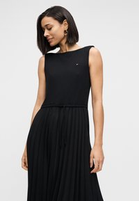 Μαύρο αμάνικο φόρεμα με ραβδωτή υφή, ελαστική μέση και πιετέ φούστα. Μικρό λογότυπο στο στήθος.