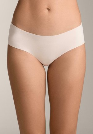 Vrouw die naadloze beige hipsterondergoed met gladde randen draagt, getoond van de taille tot halverwege de dij, tegen een neutrale achtergrond.