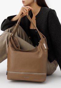 Pruun nahast õlakott, millel on siledat tekstuuri, lukuga tasku ja logosümbol. Laia, reguleeritava rihmaga ning mugav, lohvakujuline disain.