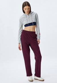 Sudadera gris recortada con una capa media en contraste en azul marino y pantalones de chándal burdeos con cintura elástica. Zapatillas blancas con suelas de goma.