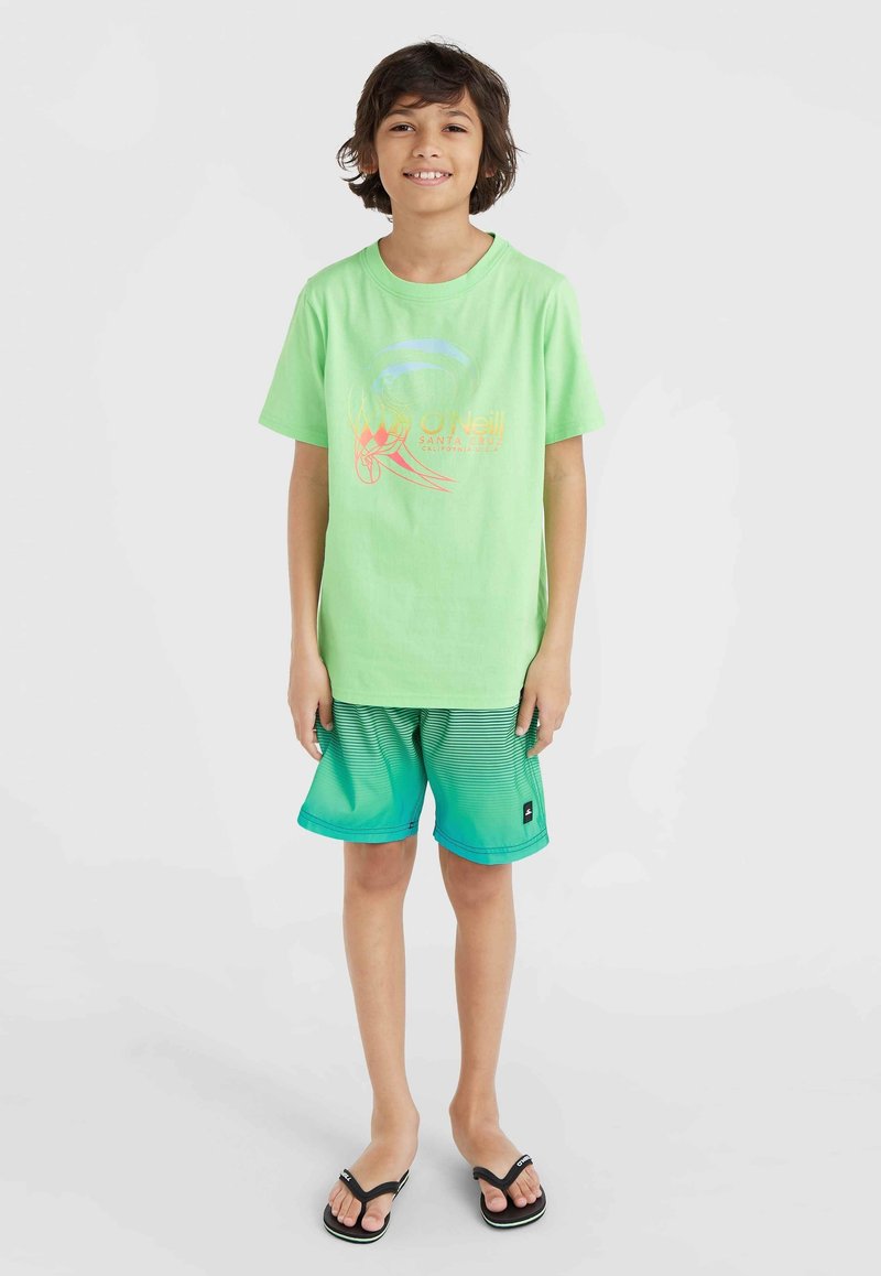 Mintgrön t-shirt med en grafisk logotyp, ihop med teal-gradient shorts med horisontella ränder. Svarta flip-flops fulländar outfiten.