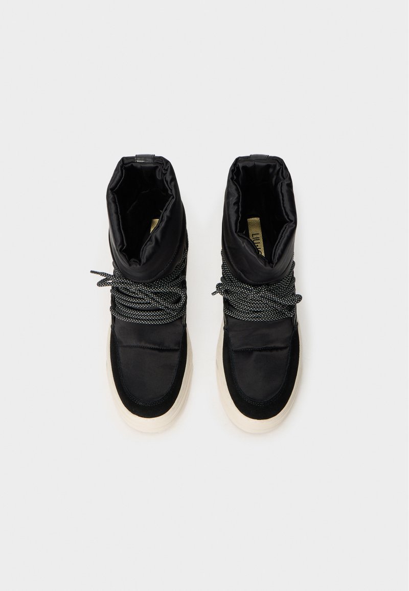 Botines negros con un acabado satinado, que presentan una parte superior fruncida, cordones grises en contraste y una gruesa suela de goma beige.