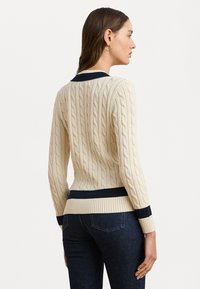 Κρεμ πουλόβερ με πλέξη καλωδίων και σκούρο μπλε ριμπ κολάρο και στρίφωμα. Διαθέτει μακριά μανίκια και εφαρμοστή γραμμή, αναδεικνύοντας χαρακτηριστικά υφής μοτίβα.