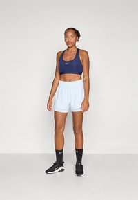 Marineblauwe sportbeha met wit Nike-logo, lichtblauwe korte broek, zwarte sportschoenen en zwarte enkelsokken. Glad materiaal, aansluitend ontwerp.