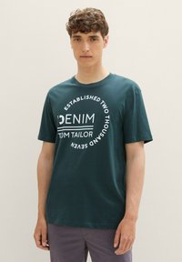 Camiseta de algodón verde azulado con cuello redondo, que presenta un estampado gráfico blanco que dice "DENIM ESTABLISHED TWO THOUSAND SEVEN" en un diseño circular.