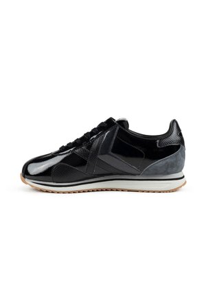 Zapatilla baja negra con paneles brillantes y texturizados, cordones negros, entresuela blanca y suela exterior ranurada de color marrón claro.