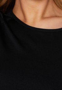 Černý krátký rukáv s hladkým, měkkým povrchem. Má kulatý výstřih a jemné švy podél okrajů.