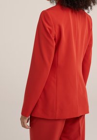 Červený přizpůsobený blazer se strukturovaným designem, dlouhými rukávy a hladkou texturou. Obsahuje jeden zadní rozvent a minimalistický styl.