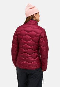 Bordeauxkleurige pufferjack met een geborduurd golfpatroon, hoge kraag en een gladde, glanzende afwerking. Gepaard met een lichtroze beanie.