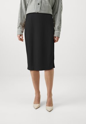 Gonna a matita nera realizzata in tessuto morbido, lunghezza al ginocchio, con spacco laterale. Abbinata a décolleté beige a punta e una camicia a righe a maniche lunghe.