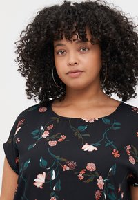 Black blouse with floral pattern featuring pink and green accents. Round neckline and short sleeves. Lightweight fabric with smooth texture.