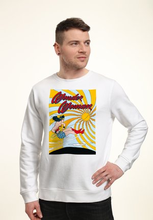 Biała bluza z kolorowym nadrukiem przedstawiającym Wonder Woman w akcji, z niebieskimi włosami, czerwonymi butami i żywym tłem w postaci żółtej eksplozji słońca.