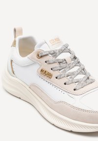 Sneaker bianco con accenti in suede beige, dettagli testurizzati, hardware dorato e lacci grigi. Presenta una suola arrotondata per un migliore comfort.