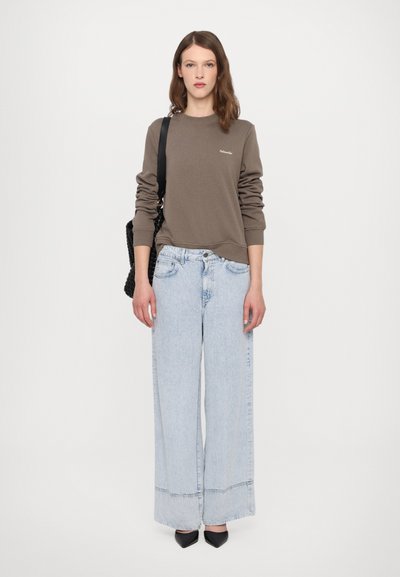 Brun genser med lange ermer, lyseblå vide jeans og svarte spisse hæler. Svart håndveske med vevet tekstur.