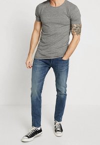 Grå T-shirt med korta ärmar och rund halsringning, kombinerad med blå jeans och svarta sneakers med vita snören och öljetter.