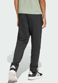 Černé tepláky s tapered střihem, měkká textura, v kombinaci s černobílými teniskami se třemi pruhy. Minimalistické značení.