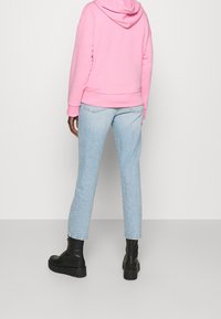 Felpa con cappuccio rosa abbinata a jeans dritti blu chiaro e stivali neri alla caviglia, mostrando una superficie liscia e una vestibilità rilassata.