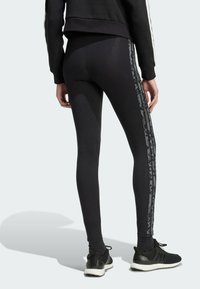 Black leggings with a smooth texture, featuring a contrasting gray side stripe with a subtle pattern. Pairing with black athletic shoes.