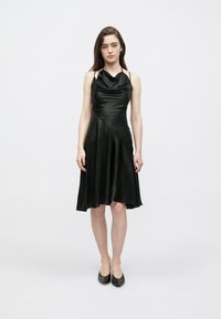 Μαύρο αμάνικο φόρεμα από απαλό ύφασμα με ντραπαριστό λαιμόκοψη τύπου κασκόλ και ασύμμετρο φόρεμα που φτάνει πάνω από τα γόνατα.