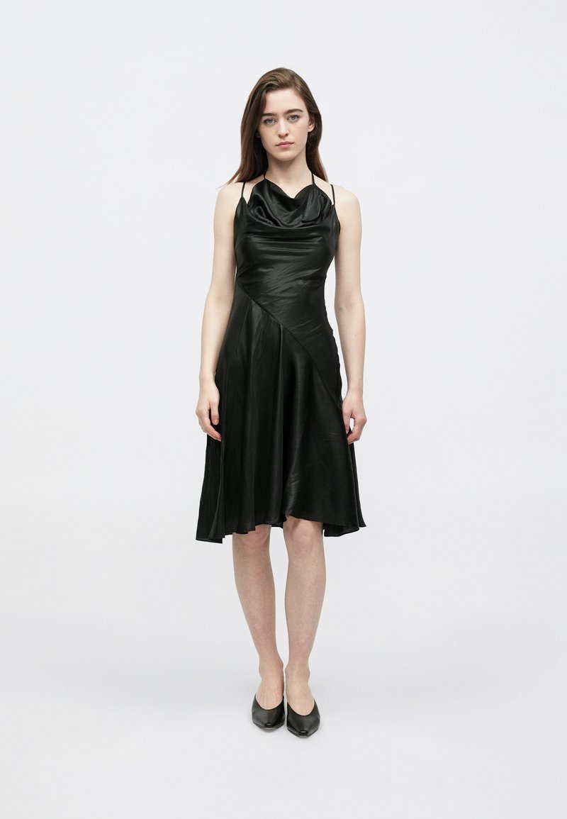 Sort ærmeløs kjole i glat stof med en draperet, halstørklignende halsudskæring og en asymmetrisk nederdel, der falder over knæene.