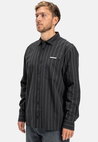 Zwart en grijs gestreepte langearm shirt met een knoopsluiting, voorzien van een borstzak en logodetail aan de zijkant. Gemaakt van katoen.