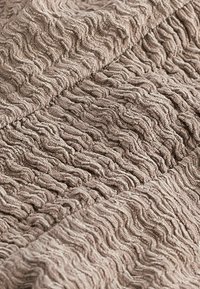 Tissu texturé beige avec un motif ondulé. Matériau doux et pelucheux avec un design en relief, montrant une profondeur et une dimension subtiles.