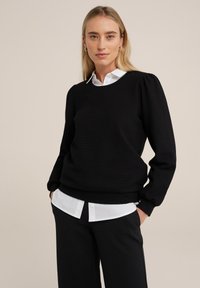 Pullover negru texturat, cu mâneci lungi, decolteu rotund și un tiv ajustat, peste o cămașă albă cu guler. Design simplu și clasic.