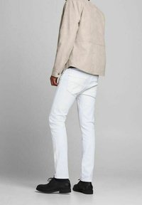 Mans ljusgrå mockajacka, vita slim-fit jeans och svarta dressade skor. Bakifrån visar den mjuka texturer och klassisk design.