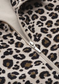Leopardprint stof in beige met zwarte en bruine vlekken, voorzien van een zilveren rits langs de naad die het gestructureerde oppervlak benadrukt.