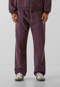 Lilla sweatpants med en afslappet pasform, prydet med vertikale syninger, elastisk talje og snor. Kombineret med hvide og grå sneakers.