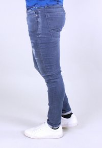 Slim-fit grå denimjeans med en lätt slitagedetalj, bärs med vita sneakers. Tyget ser stretchigt ut för komfort.