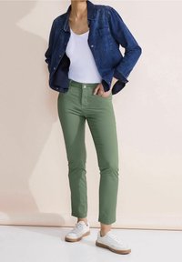 Jeansjacka, vit linne, gröna slim-fit byxor och vita sneakers. Enkelt design, medelblått tyg, med framfickor och silverknappar.