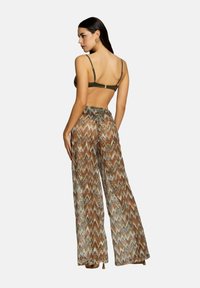 Pantaloni bronze e marroni con motivo a zigzag, abbinati a un reggiseno verde a spalline. Tessuto morbido con una vestibilità rilassata.