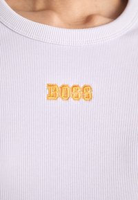 Ljuslila ribbad t-shirt med rund halsringning och broderad "BOSS"-logotyp i gult över bröstet. Slät textur, figursydd design.