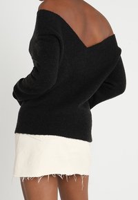 Mustat olkapään paljastavat neuleet, jotka on valmistettu pehmeästä materiaalista. Siinä on pitkät hihat ja rento istuvuus, yhdistetty valkoiseen frillaiseen farkkuhameeseen.