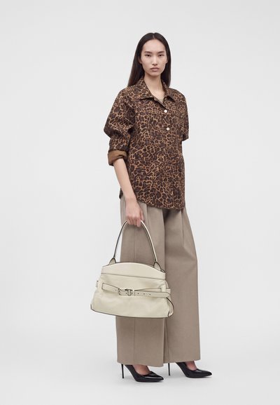 Femme portant une veste imprimé léopard et un pantalon large beige, tenant un grand sac à main blanc et portant des talons hauts noirs.