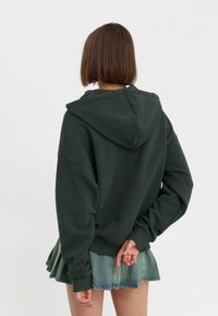 Donkergroene hoodie van zachte stof, met een capuchon, verlaagde schouders en een relaxte pasvorm, gecombineerd met een denim rok.