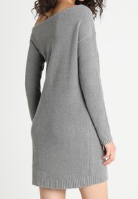 Graues schulterfreies, geripptes Strickkleid mit langen Ärmeln, das eine figurbetonte Silhouette und einen leicht zulaufenden Saum aufweist. Weicher Stoff und lässiges Design.