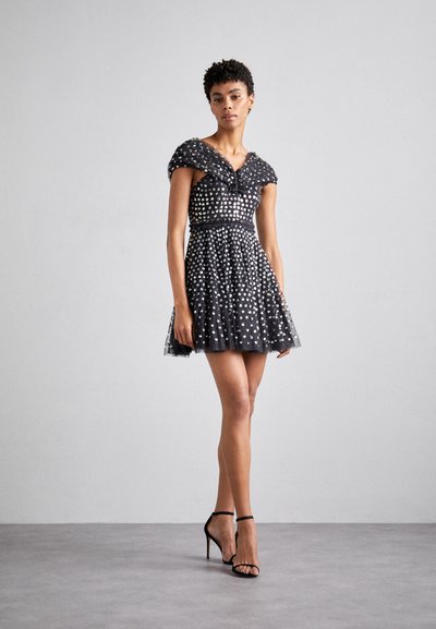 Rochie din tulle negru cu mâneci scurte, embellismente argintii, talie strânsă, fustă evazată și detalii semitransparente, asortată cu sandale negre cu bretele.