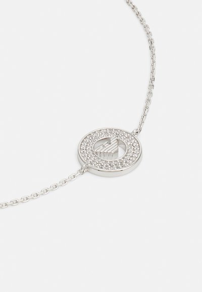 Silberne Halskette mit einem runden Anhänger, der eine strukturierte Mitte und einen umlaufenden Rand mit eingelegten kleinen Kristallen aufweist. Das Kettendesign ist gleichmäßig und filigran.