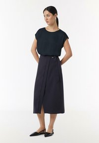 Czarny top z krótkim rękawem w zestawieniu z granatową spódnicą o wysokim stanie, z rozcięciem z przodu, paskiem w talii i eleganckimi czarnymi balerinami.