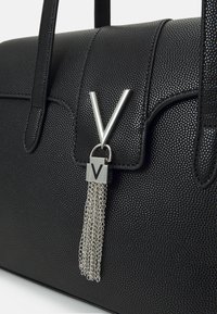 Crna teksturirana torba s metalnim V-oblika kopčanjem i detaljem lančane rese, s kratkim drškama i strukturiranim dizajnom.