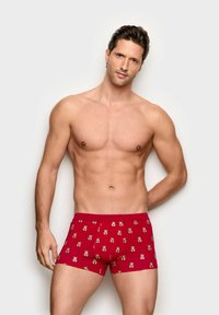 Red boxer shorts made of soft fabric featuring a repeated teddy bear pattern. The design includes a fitted shape and elastic waistband.
