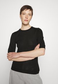 Black short-sleeve knit top with a round neckline and ribbed hem. Smooth texture with a fitted silhouette.