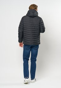 Črna puhovka s kapuco, ki ima quilted detajle in prilegajoč dizajn. V kombinaciji z modrimi trapericami in belimi supergami.