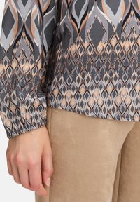 Bluzka z długim rękawem w szarym, beżowym i czarnym kolorze, z motywem diamentów i elastycznymi mankietami, w zestawieniu z miękkimi beżowymi spodniami.