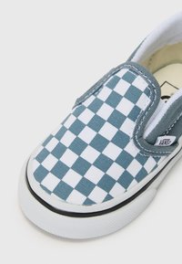 Plave i bijele kvadratične slip-on cipele napravljene od platna, s bijelim gumeni đonom i crnim obrubom. Oznaka s Vans logotipom.