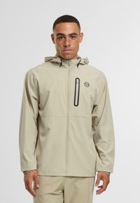 Světlý béžový nepromokavý kabát se zipem vpředu, nastavitelnou kapucí a hrudní kapsou. Hladká textura s logem na levé straně.